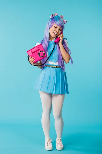 Повний вигляд азіатської аніме-дівчини, що розмовляє по телефону на синьому — стокове фото