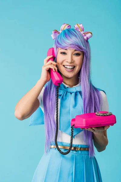 Smiling asian anime girl talking on telephone isolated on blue — Stock Photo