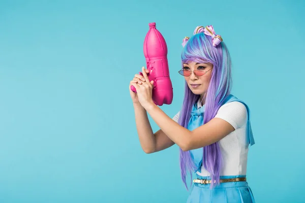 Asian anime girl in wig and glasses holding water gun isolated on blue — Stock Photo