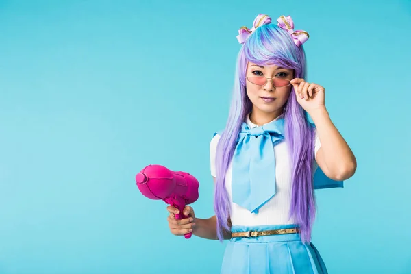 Asiático anime chica en peluca y gafas celebración agua pistola aislado en azul - foto de stock