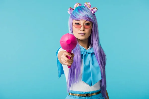 Seria asiático anime chica en peluca y gafas celebración agua pistola aislado en azul - foto de stock