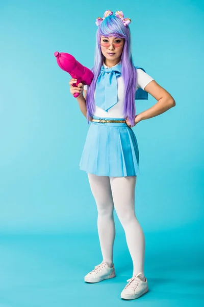 Full length view of asian anime girl in wig and glasses holding water gun on blue — Stock Photo