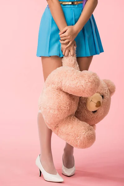 Partial view of girl in blue skirt holding teddy bear on pink — Stock Photo