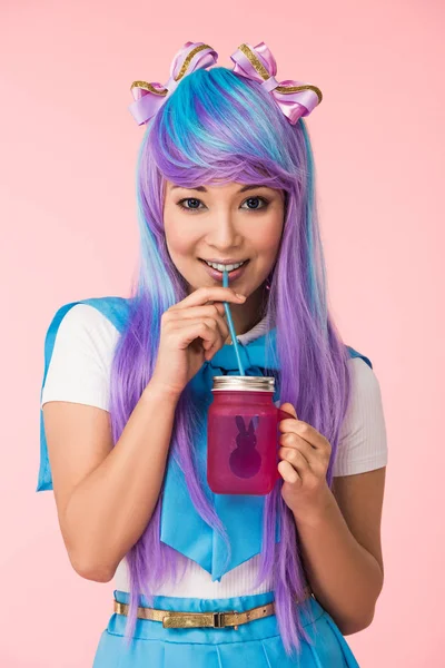 Sonriente asiático anime chica bebiendo bebida aislado en rosa - foto de stock
