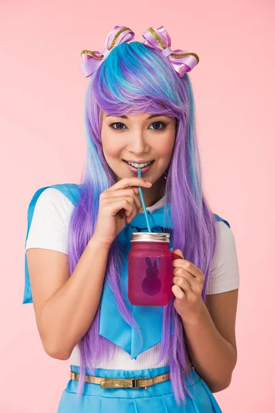 Smiling asian anime girl drinking beverage isolated on pink — Stock Photo