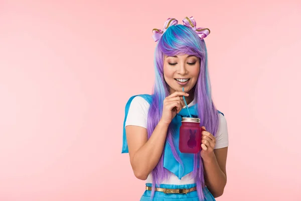 Улыбающаяся аниме девушка в парике, пьющая напиток, изолированный на розовый — стоковое фото