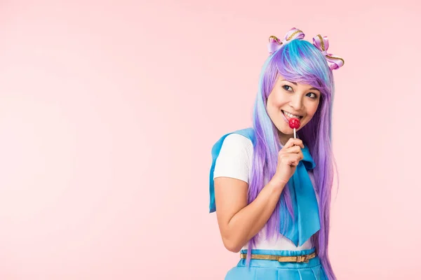 Happy asian otaku girl in wig eating lollipop isolated on pink — Stock Photo