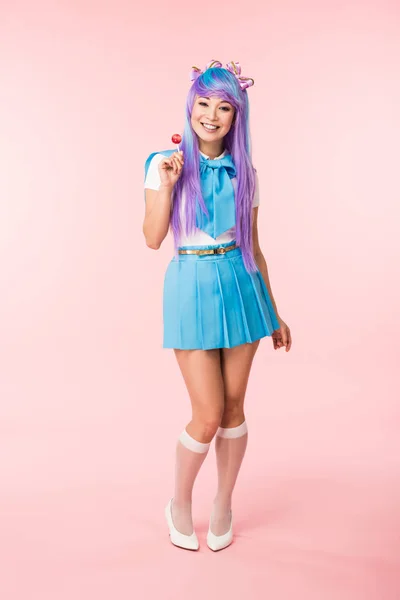 Full length view of smiling asian otaku girl holding lollipop on pink — Stock Photo