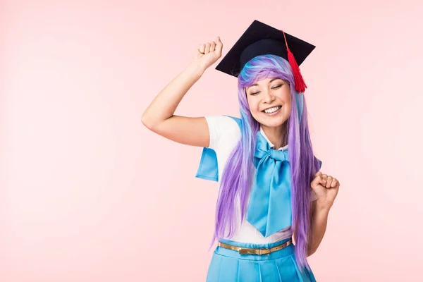 Anime girl in purple wig and academic cap smiling isolated on pink — Stock Photo