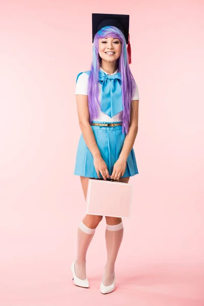 Pleine longueur vue de sourire anime fille en chapeau académique tenant mallette sur rose — Photo de stock