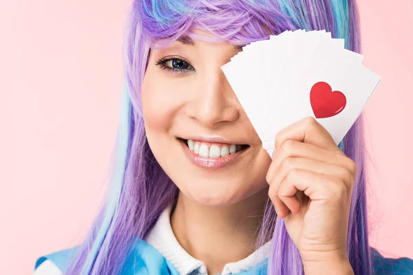 Charming asian anime girl in purple wig holding cards with heart isolated on pink — Stock Photo