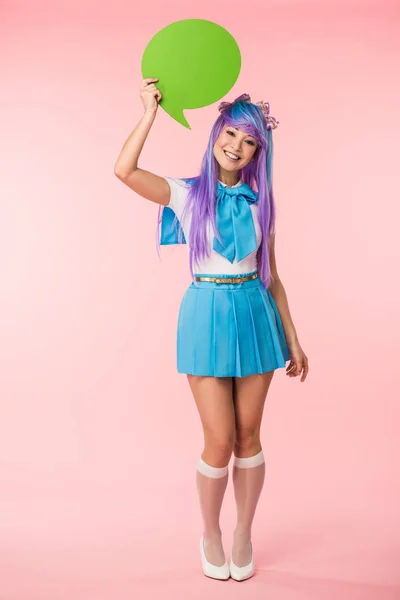 Full length view of smiling asian anime girl holding green speech bubble on pink — Stock Photo