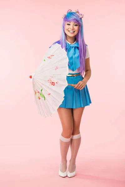 Full length view of smiling asian anime girl holding paper umbrella on pink — Stock Photo