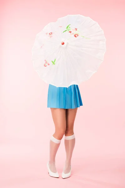 Повнометражний вигляд дівчини в білих шкарпетках на колінах, що тримає паперову парасольку на рожевому — стокове фото