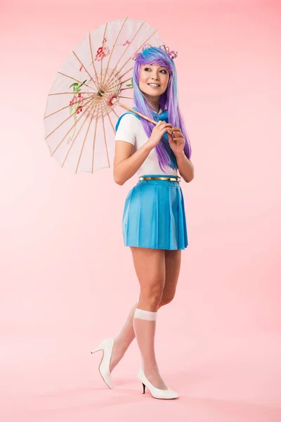 Comprimento total vista de sorrir asiático anime menina segurando papel guarda-chuva em rosa — Fotografia de Stock