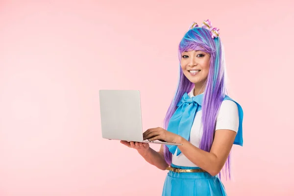 Sorrindo anime menina em peruca roxa usando laptop isolado em rosa — Fotografia de Stock