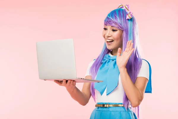 Joyful asiático anime chica saludando mano en la pantalla del ordenador portátil en rosa - foto de stock