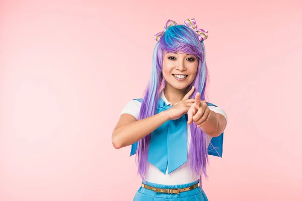 Sourire asiatique anime fille en pourpre perruque pointant avec doigt à caméra isolé sur rose — Photo de stock