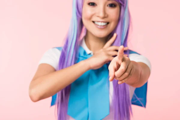Sonriente asiático anime chica en púrpura peluca apuntando con el dedo a la cámara aislado en rosa - foto de stock