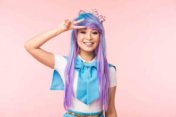 Blissful asian anime girl in purple wig showing peace sign isolated on pink — Stock Photo