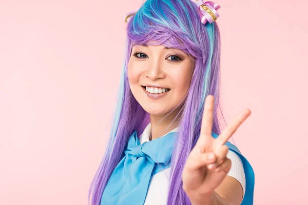 Beata ragazza anime asiatica in parrucca viola mostrando segno di pace isolato su rosa — Foto stock