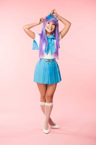 Vista completa de la bonita chica de anime en peluca y traje de marinero de pie en rosa - foto de stock