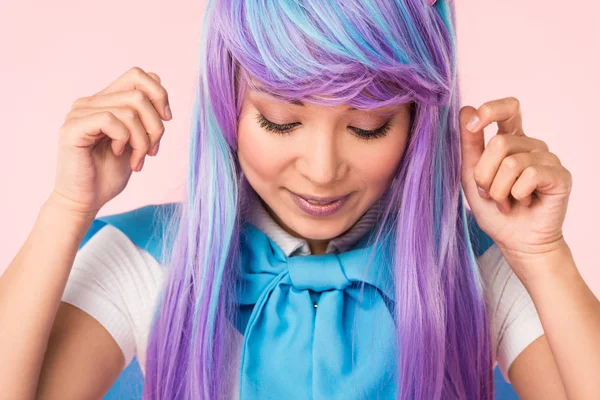Sonriente chica de anime en peluca mirando hacia abajo aislado en rosa - foto de stock