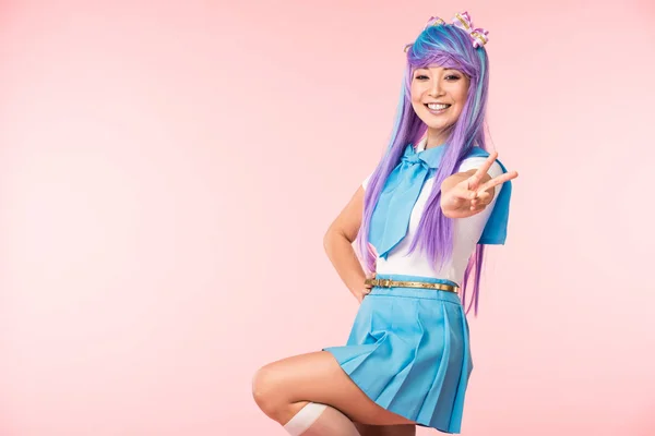 Glücklich asiatische anime Mädchen steht auf einem Bein und zeigt Peace Zeichen auf rosa — Stockfoto