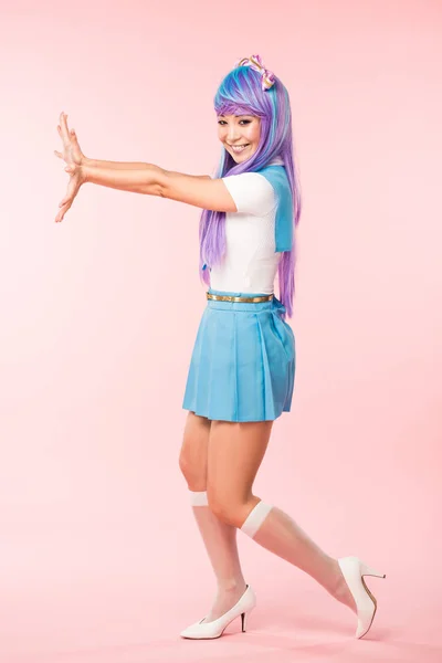 Vista completa de la chica otaku sonriente en peluca púrpura posando en rosa - foto de stock