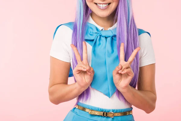 Vista cortada da menina anime sorridente em peruca roxa mostrando sinais de paz isolados em rosa — Fotografia de Stock