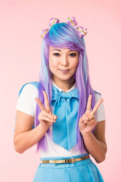 Smiling anime girl in purple wig showing peace signs isolated on pink — Stock Photo