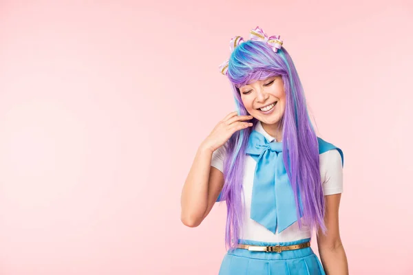 Linda chica de anime en peluca sonriendo con los ojos cerrados aislados en rosa - foto de stock