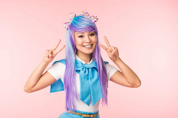 Fröhliche asiatische Anime-Mädchen in lila Perücke zeigt Friedenszeichen isoliert auf rosa — Stockfoto