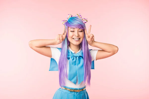 Chica anime feliz en peluca púrpura mostrando signos de paz con los ojos cerrados en rosa - foto de stock