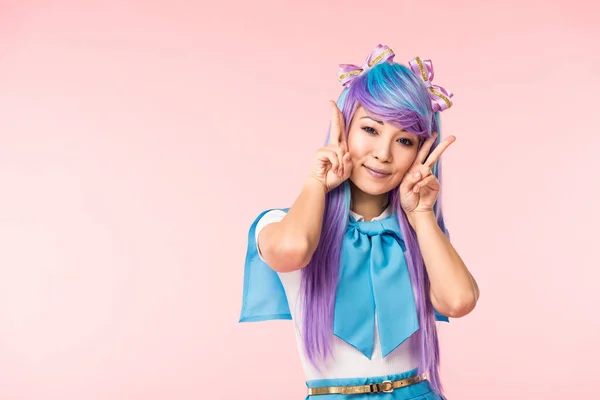 Hübsche asiatische Anime-Mädchen in lila Perücke zeigt Friedenszeichen isoliert auf rosa — Stockfoto