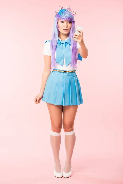 Вид в полный рост на аниме девочки, держащей смартфон на розовом фоне — стоковое фото