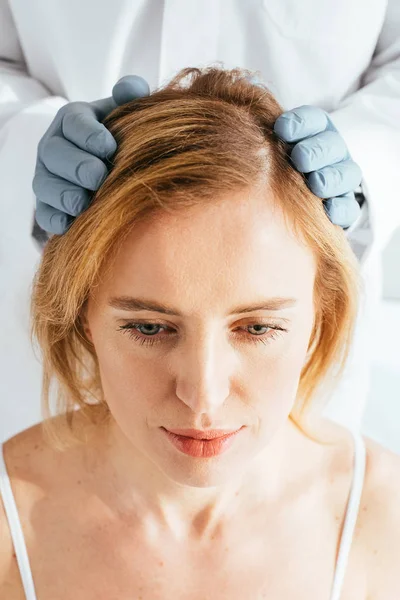 Vista recortada del dermatólogo en guantes de látex examinando el cabello del paciente - foto de stock