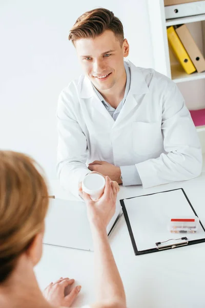 Overhead view of cheerful doctor giving container with cosmetic cream to patient — Stock Photo