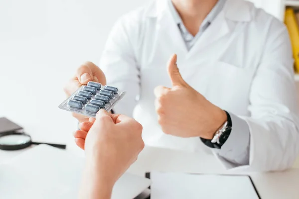 Vue recadrée du médecin montrant pouce vers le haut tout en donnant des pilules au patient — Photo de stock