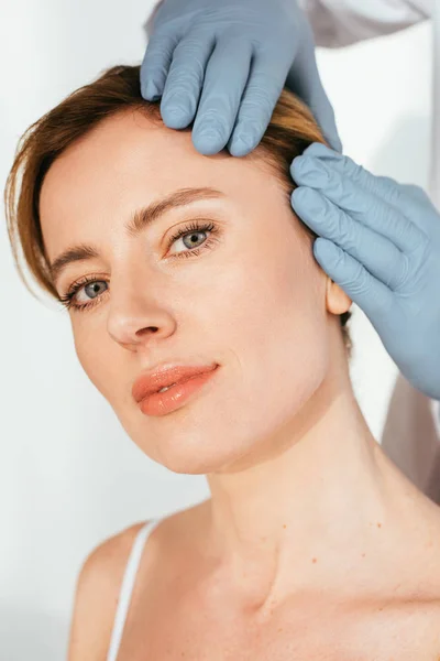 Cropped view of dermatologist in latex gloves examining hair of attractive patient on white — Stock Photo
