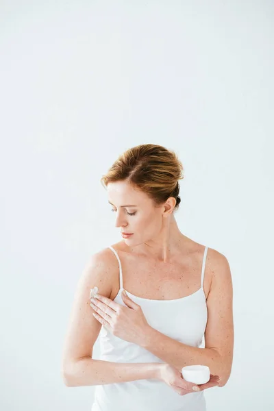 Mulher atraente com doença de pele segurando recipiente e aplicando creme cosmético no branco — Fotografia de Stock