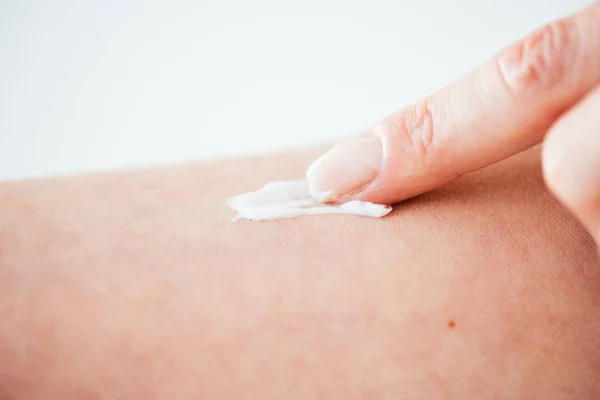 Vista cortada da mulher aplicando creme cosmético com o dedo no branco — Fotografia de Stock