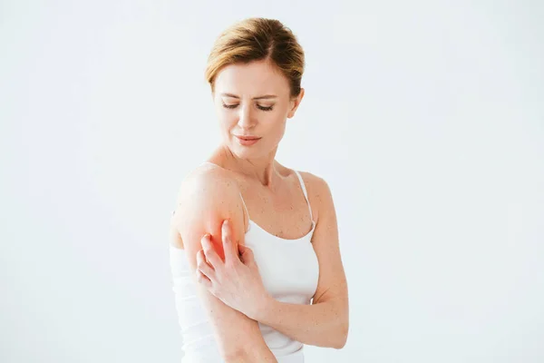 Красивая аллергическая женщина царапает красную кожу на руке, стоя на белом — стоковое фото