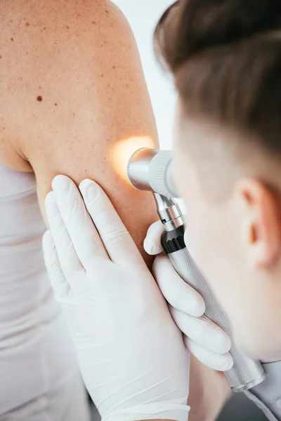 Vista recortada del dermatólogo que sostiene el dermatoscopio mientras examina a la mujer - foto de stock