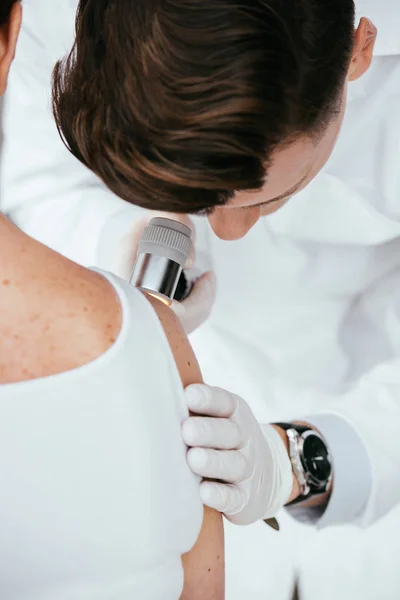 Visão cortada de dermatologista segurando dermatoscópio enquanto examina paciente com melanoma — Fotografia de Stock