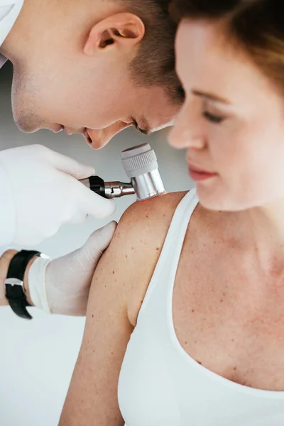 Enfoque selectivo del dermatólogo que sostiene el dermatoscopio mientras examina al paciente con melanoma - foto de stock