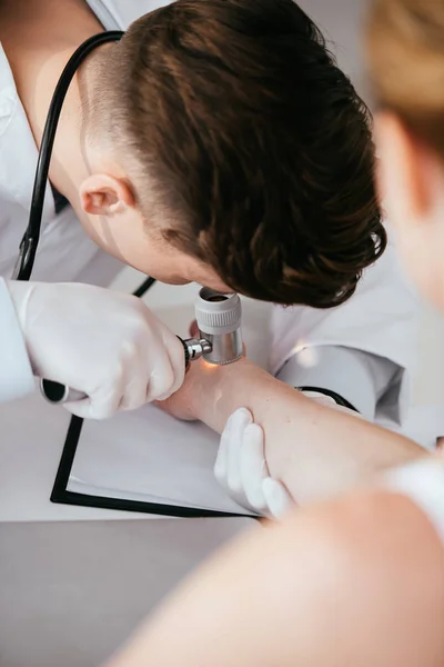 Foco seletivo do dermatologista segurando dermatoscópio e examinando a mulher com melanoma — Fotografia de Stock