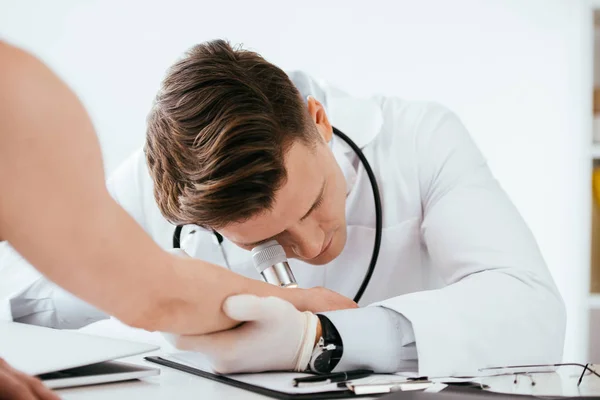 Selective focus of dermatologist examining hand of woman while holding dermatoscope — Stock Photo