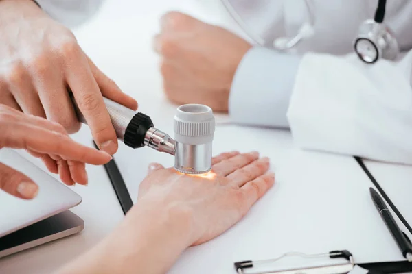 Ausgeschnittene Ansicht eines Dermatologen, der die Hand einer Frau untersucht, während sie ein Dermatoskop in der Klinik hält — Stockfoto