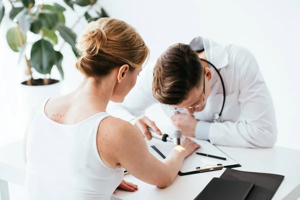 Вибірковий фокус жінки, що дивиться на дерматолога, який вивчає шкіру в клініці — стокове фото